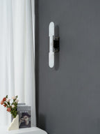 Clérachic sconce centred on a graphite wall, warm light lifting the stone against the pale curtain alongside