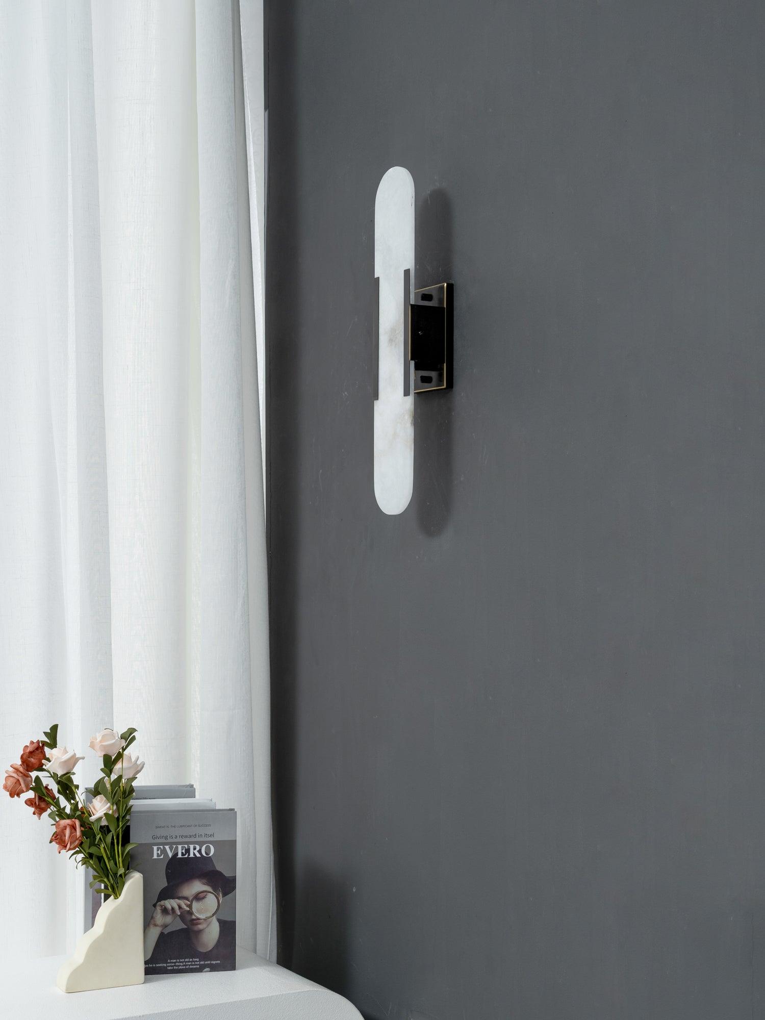 Clérachic sconce centred on a graphite wall, warm light lifting the stone against the pale curtain alongside
