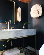The Clérachic sconce mounted over a brass-framed mirror in a navy washroom with a marble trough basin