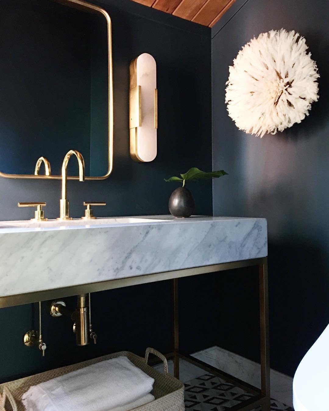 The Clérachic sconce mounted over a brass-framed mirror in a navy washroom with a marble trough basin