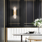 The Clérachic sconce lit on a dark panelled dining wall with brass inlay, above a white leather banquette
