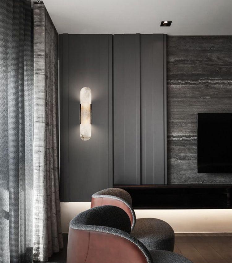 The Clérachic sconce on a grey travertine lounge wall, dark drapery and low seating around the fireplace