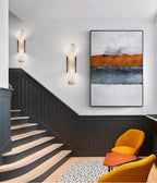 A pair of Clérachic sconces climbing a staircase wall beside an abstract canvas and dark wainscoting