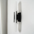 Clérachic sconce angled to reveal the black backplate and mount, a pale curtain falling behind it