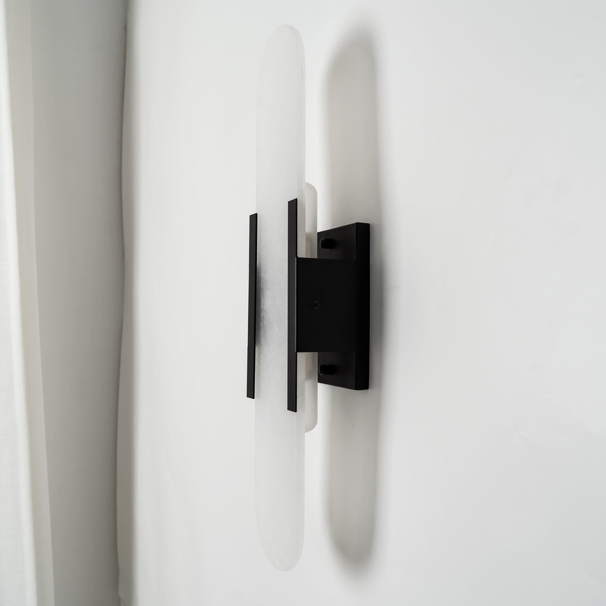 Clérachic sconce angled to reveal the black backplate and mount, a pale curtain falling behind it