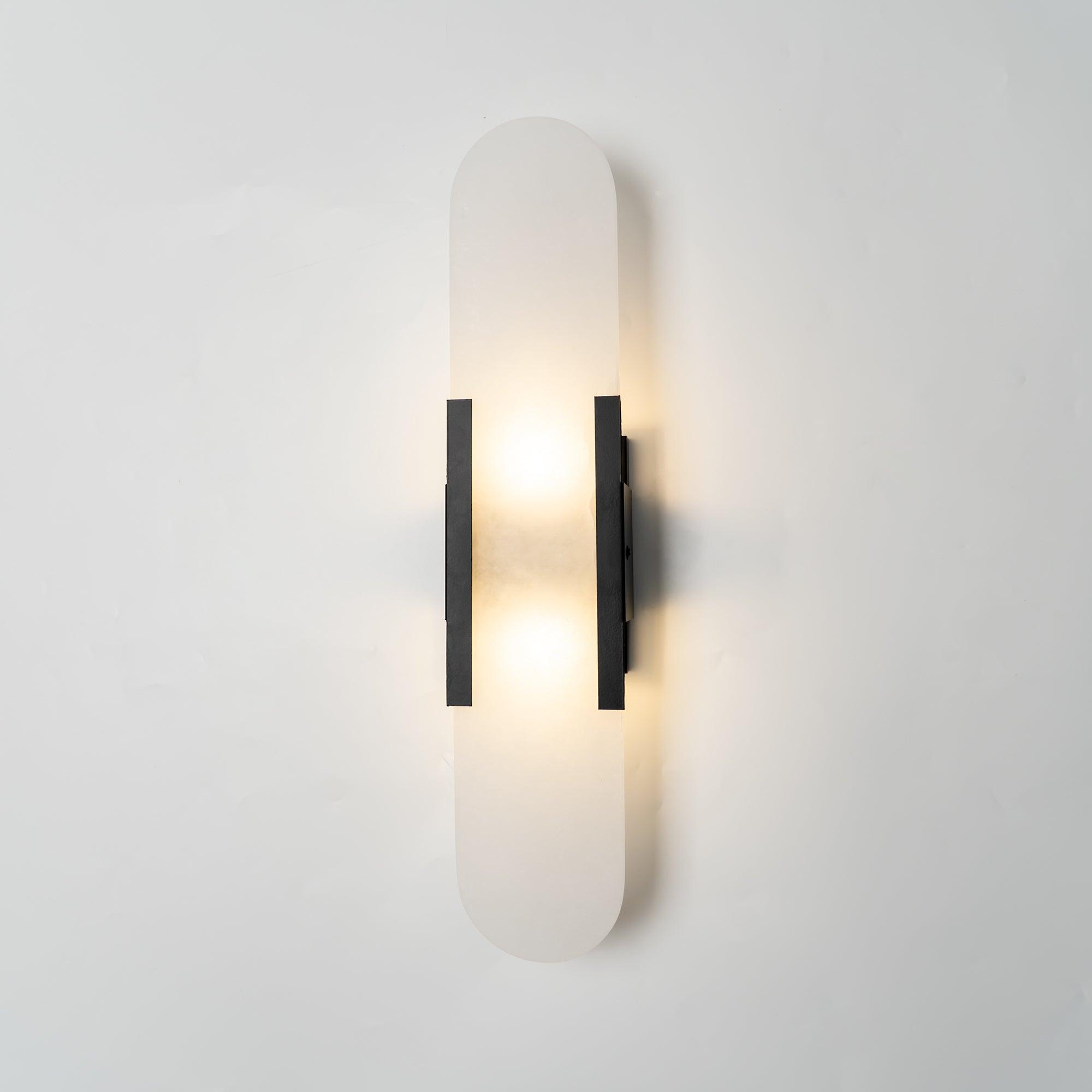 The Clérachic sconce lit head-on in black, both bulbs visible through the translucent stone capsule