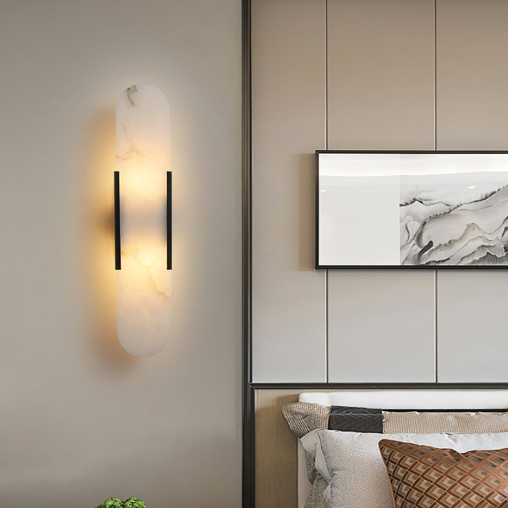 The Clérachic sconce lit on a beige panelled bedroom wall beside framed marble art and a quilted cushion