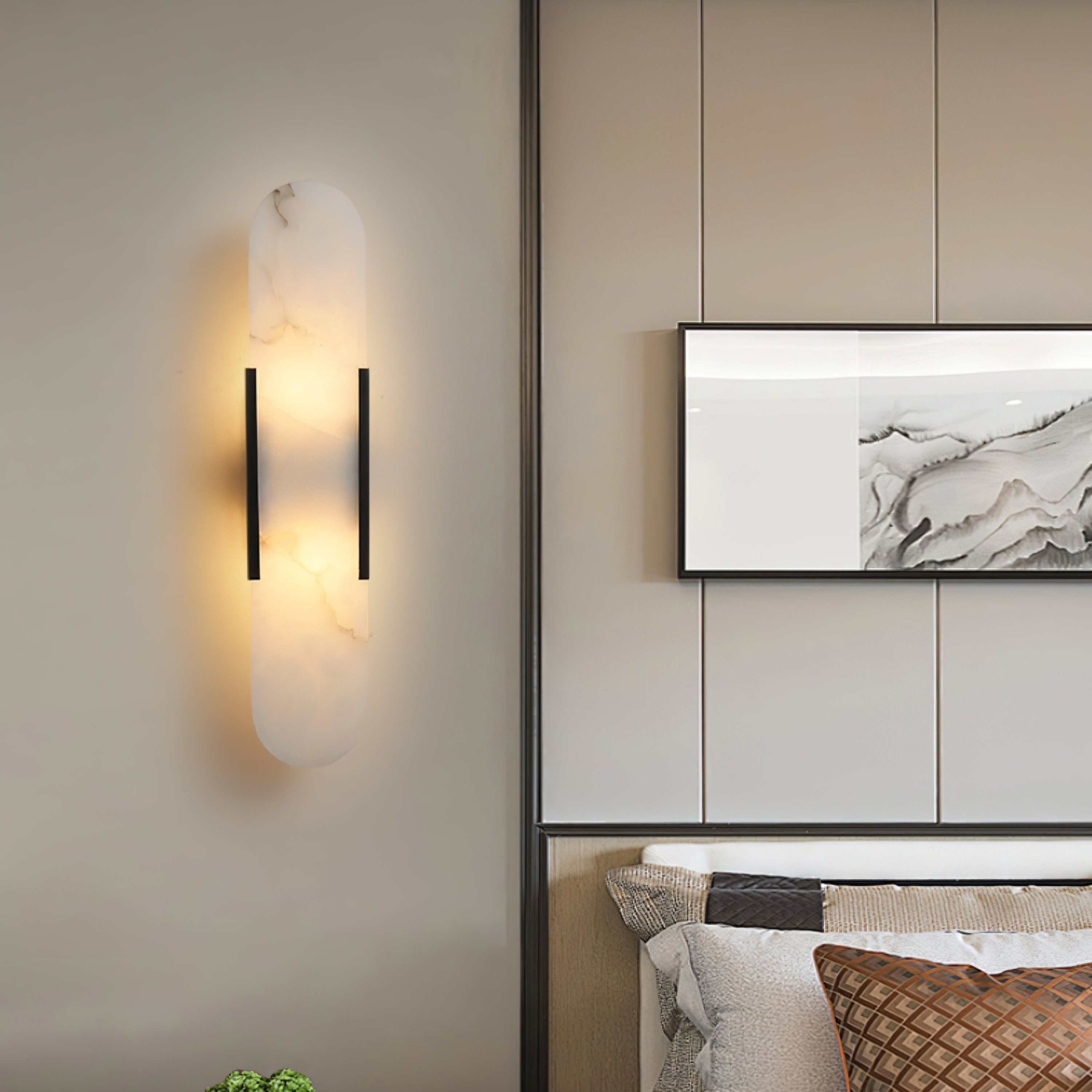 The Clérachic sconce lit on a beige panelled bedroom wall beside framed marble art and a quilted cushion