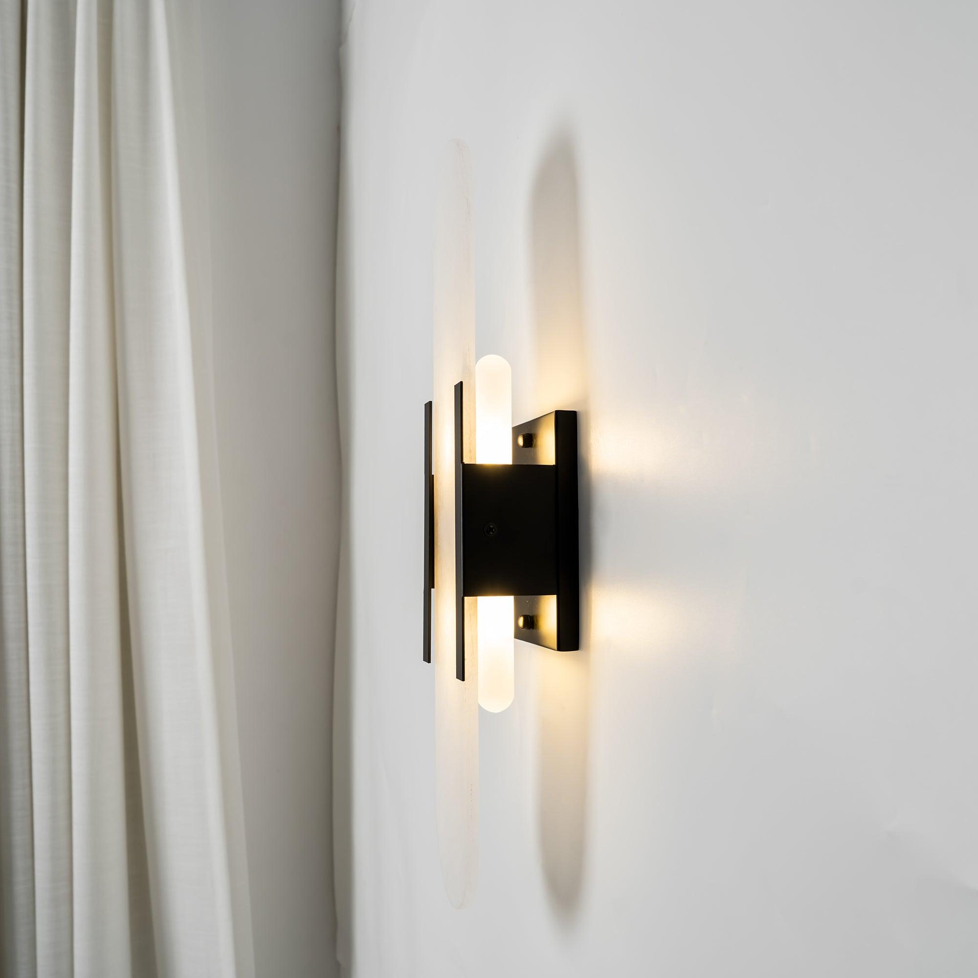 Clérachic sconce lit at an angle beside a cream curtain, light washing up and down the alabaster