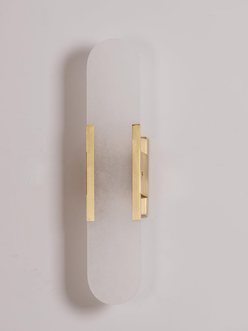 The Clérachic sconce in brass, unlit on a soft lilac-grey backdrop with the bars set low on the panel