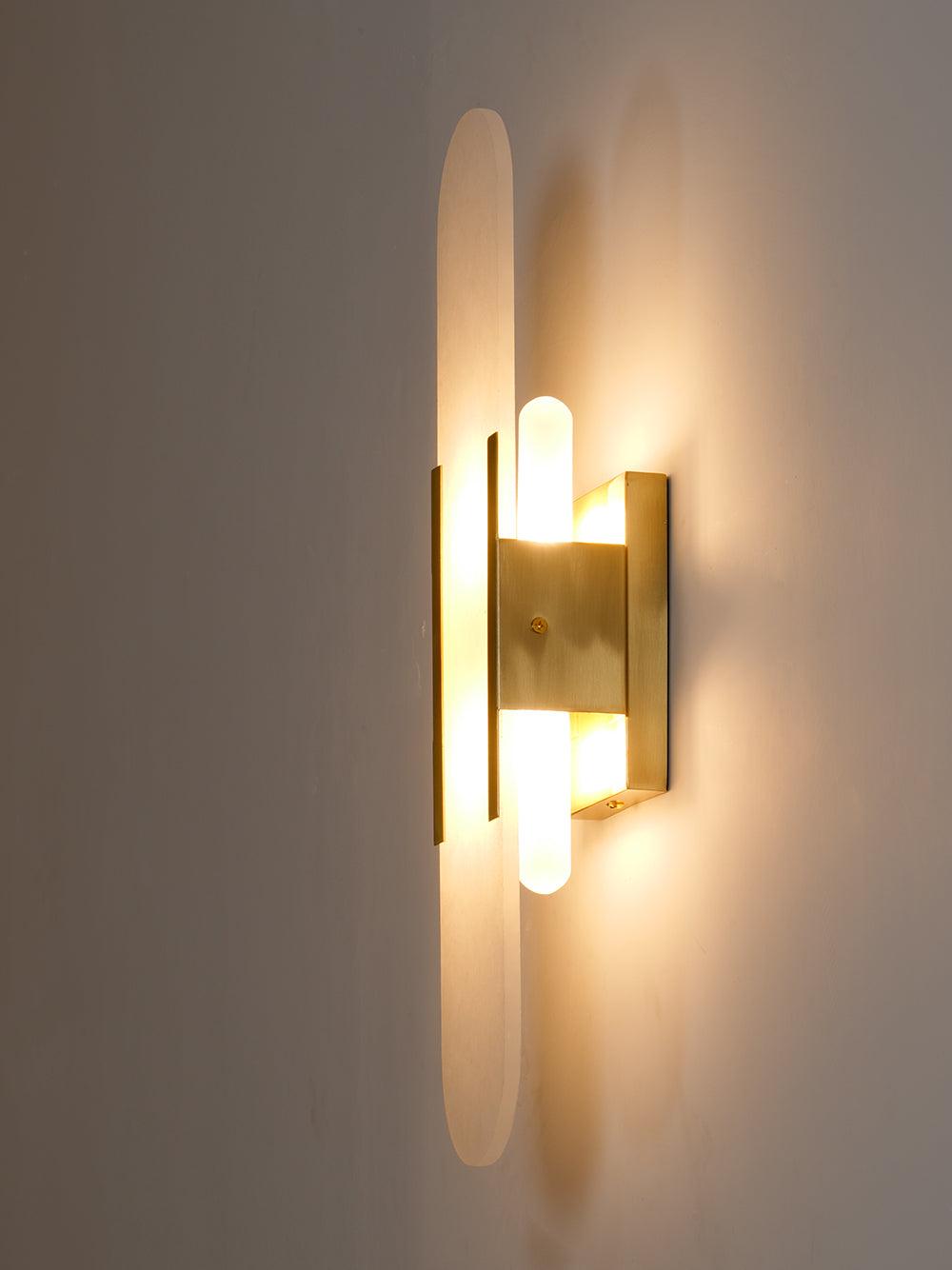 The Clérachic sconce lit against a warm dark wall, the brass body glowing amber either side of the stone