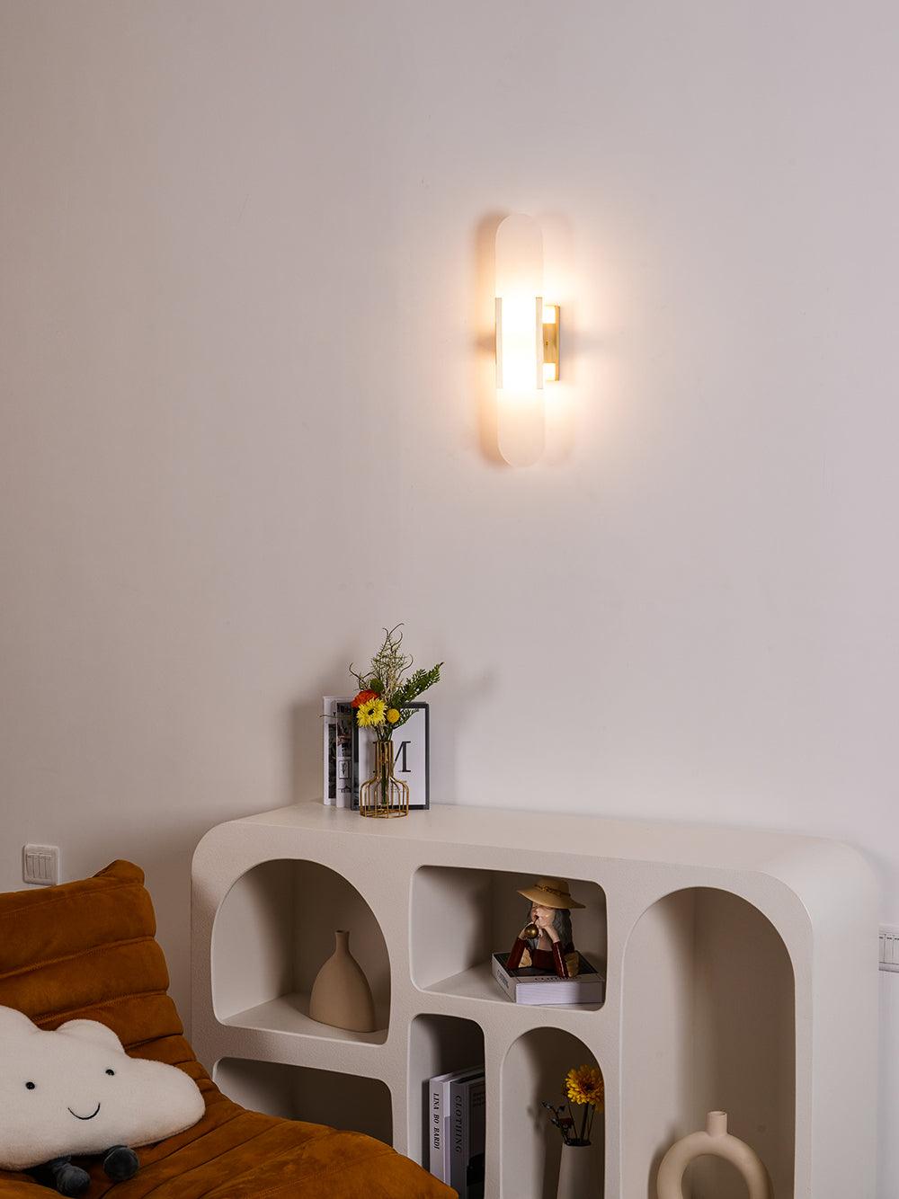 The Clérachic sconce seen wider in the same room, lighting the beige wall over curved arched shelving