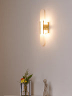 The Clérachic sconce closer on the same pale wall, brass body and lit stone above the styled shelf