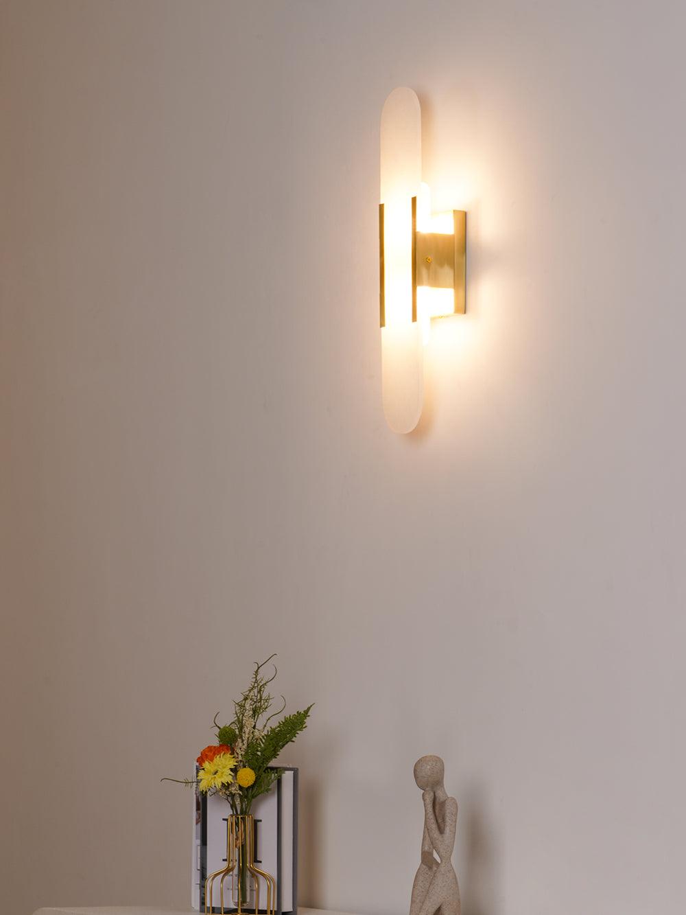 The Clérachic sconce closer on the same pale wall, brass body and lit stone above the styled shelf
