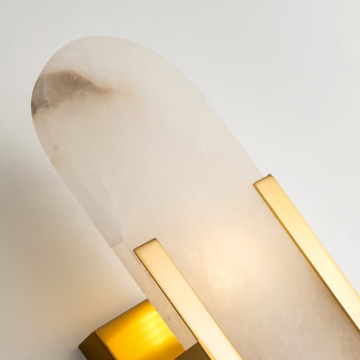 The Clérachic sconce photographed close, the rounded top of the alabaster meeting the brass bar