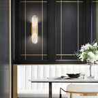 Clérachic sconce lit on a black panelled dining wall with brass trim, above a white banquette and set table