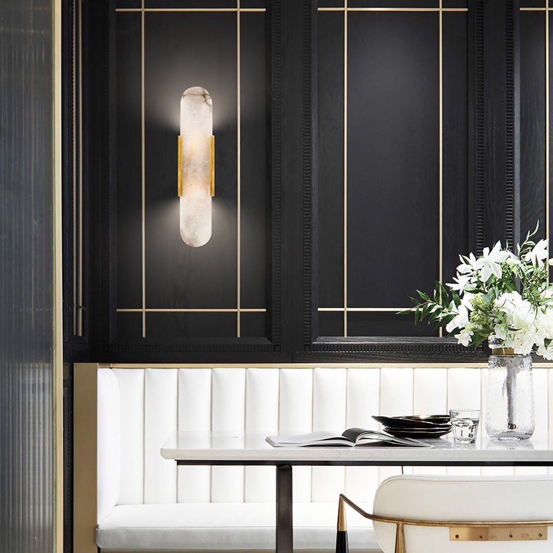 Clérachic sconce lit on a black panelled dining wall with brass trim, above a white banquette and set table