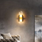 The Clérachic sconce lit on a grey plaster wall above a tufted sofa, artwork at the edge of the frame