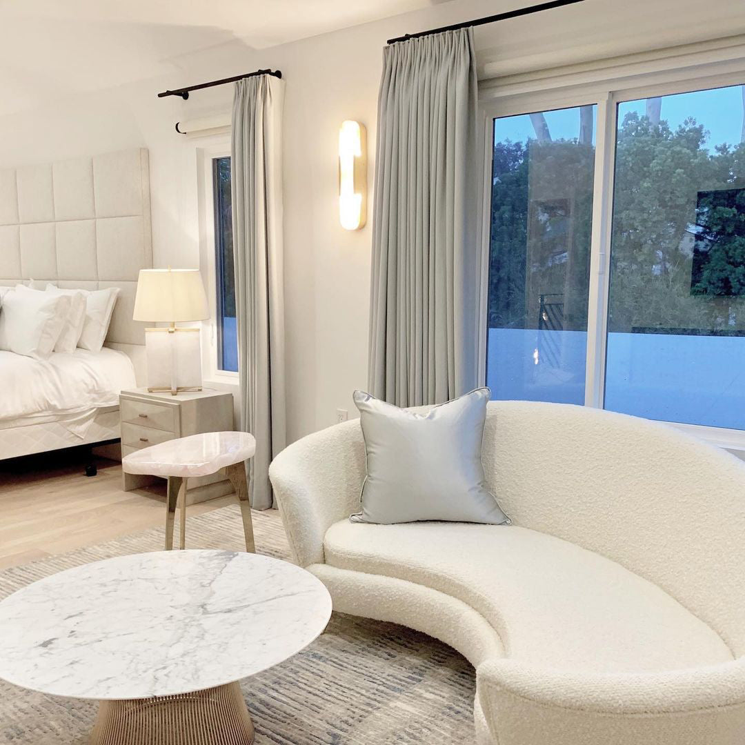 Clérachic sconce lit on a white wall in a bright lounge with a curved boucle sofa and marble table