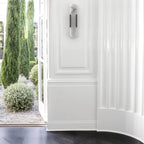 Clérachic sconce unlit on a white panelled wall, garden doors open to cypress and gravel beyond