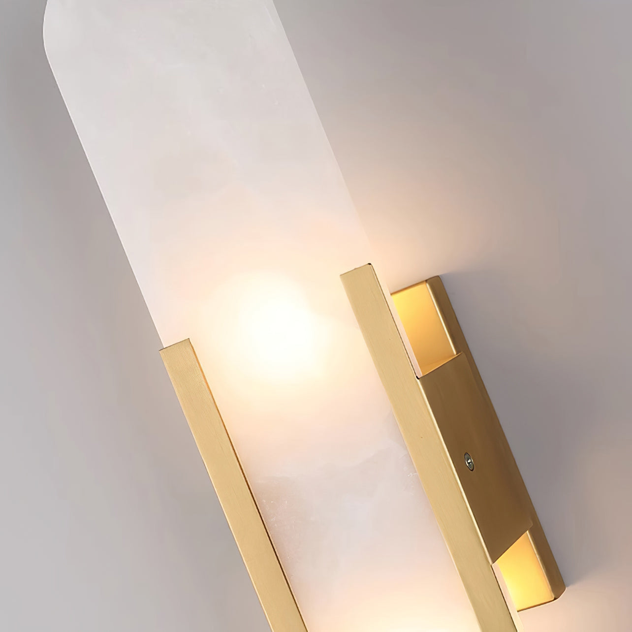 The Clérachic sconce close up from below, one bulb glowing between the brushed brass bars