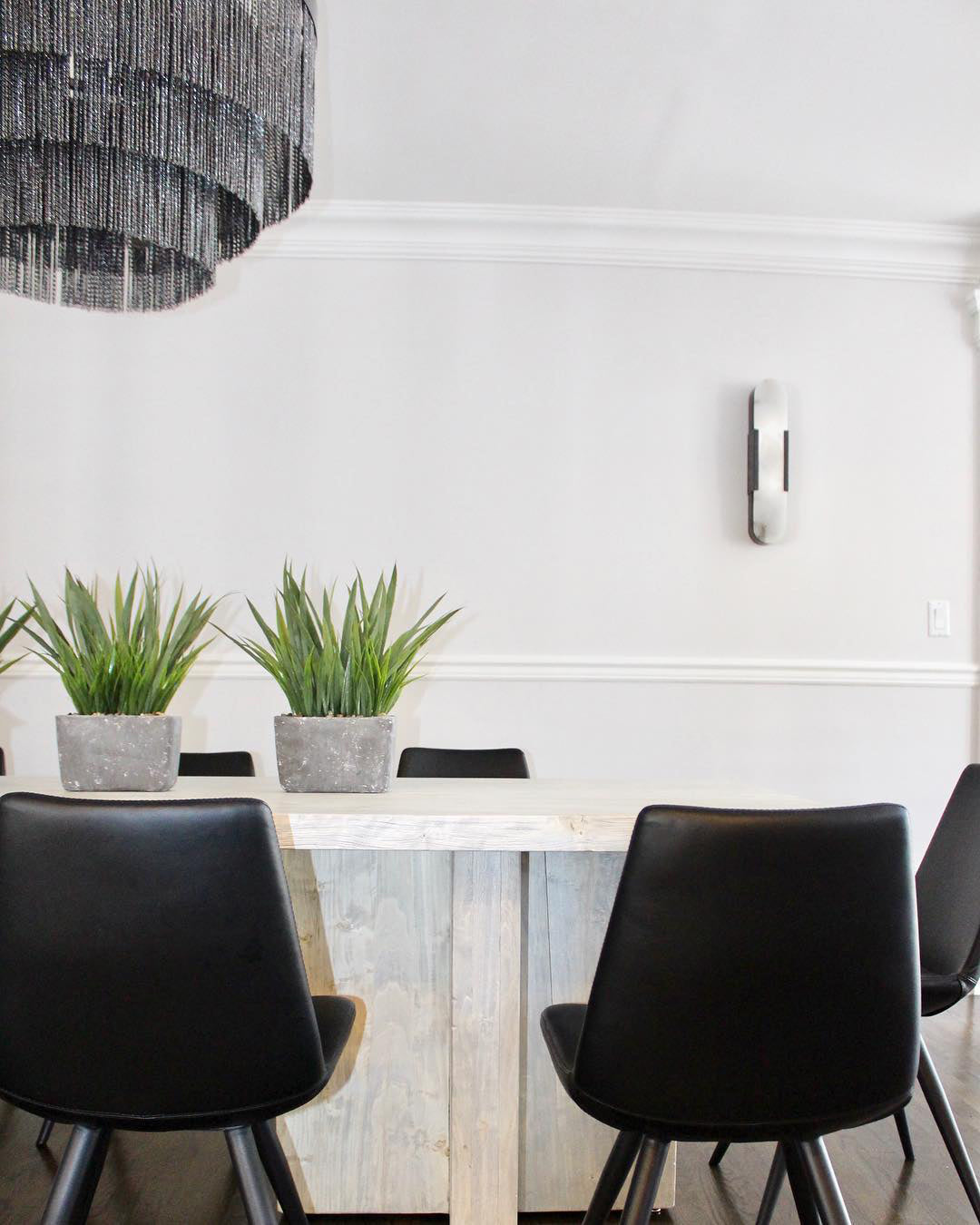 The Clérachic sconce unlit on a white dining-room wall beside potted greenery and black chairs
