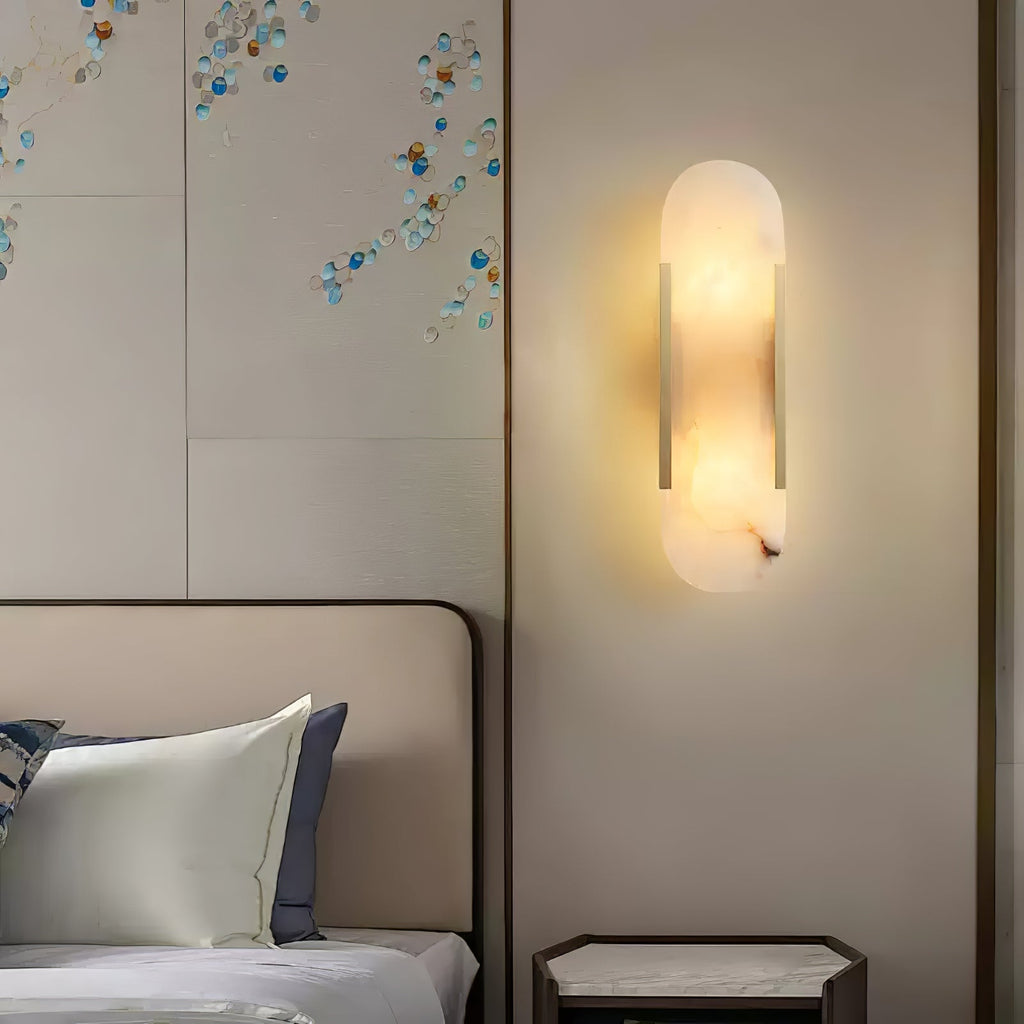 The Clérachic sconce lit on a beige panelled bedroom wall beside blue floral wall art and a nightstand