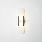 The Clérachic sconce lit softly with black bars, the stone capsule pale against a white studio wall