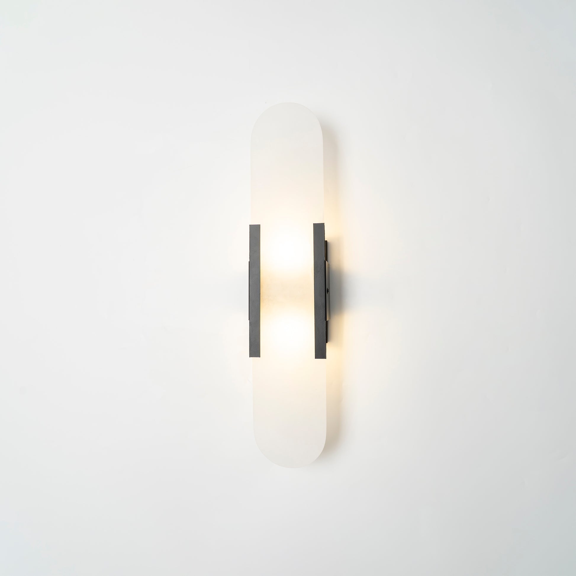 The Clérachic sconce lit softly with black bars, the stone capsule pale against a white studio wall