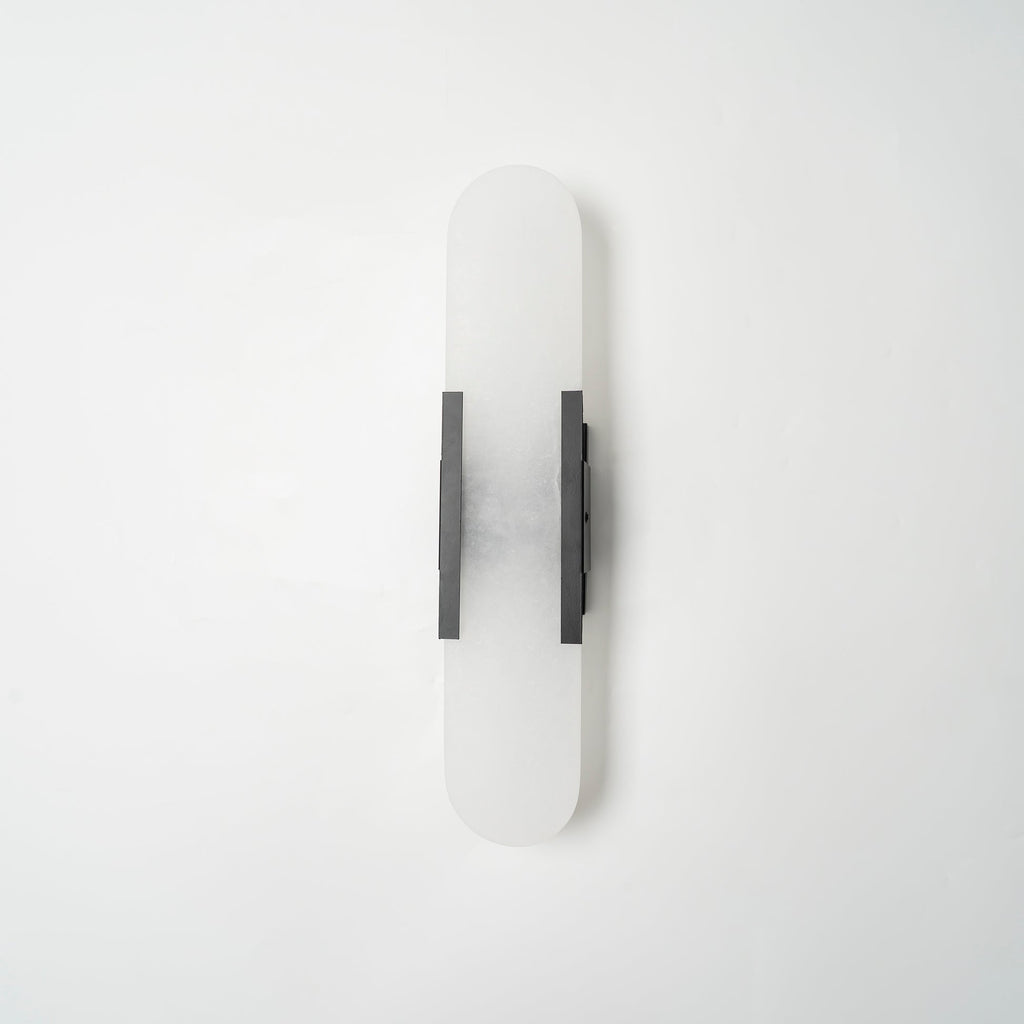 The Clérachic sconce unlit in black, shown flat-on so the full capsule proportions read clearly