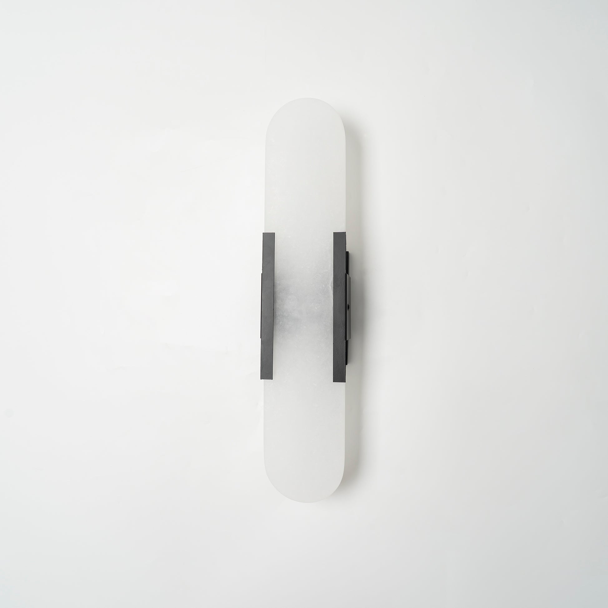 The Clérachic sconce unlit in black, shown flat-on so the full capsule proportions read clearly