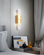 The Clérachic sconce lit on a grey panelled bedroom wall beside an armchair and a styled console