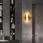 Clérachic sconce lit on a concrete wall in a dark study lined with deep timber bookshelves