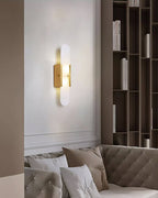 The Clérachic sconce lit on a white living-room wall above a cream tufted sofa and tall shelving