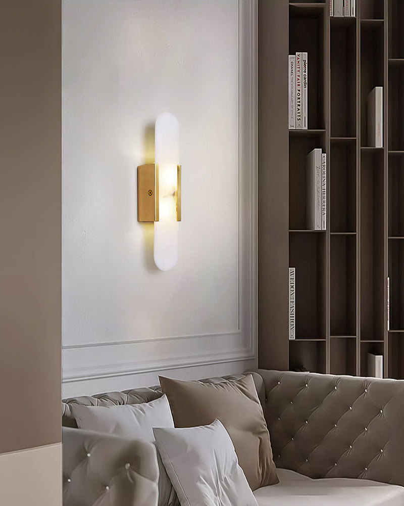 The Clérachic sconce lit on a white living-room wall above a cream tufted sofa and tall shelving