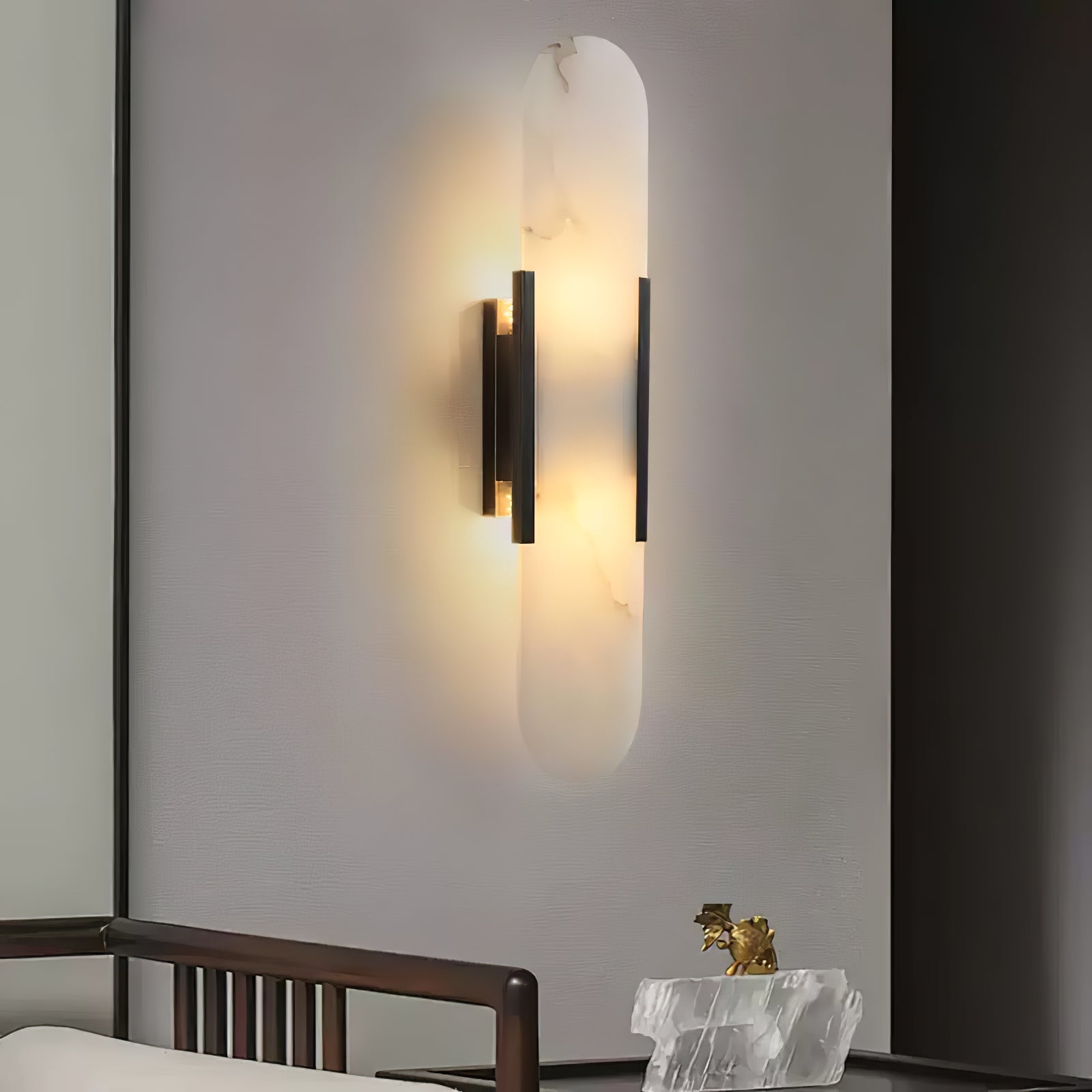 The Clérachic sconce with black bars lit on a pale wall above a wooden chair and a raw crystal