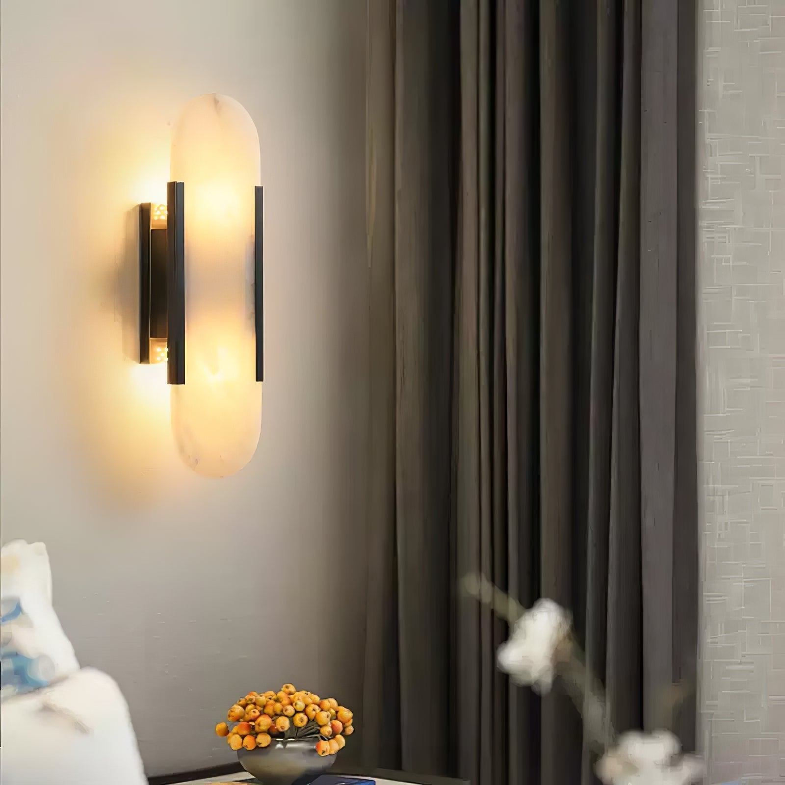Clérachic sconce lit on a pale wall next to heavy grey curtains, a bowl of orange berries beneath