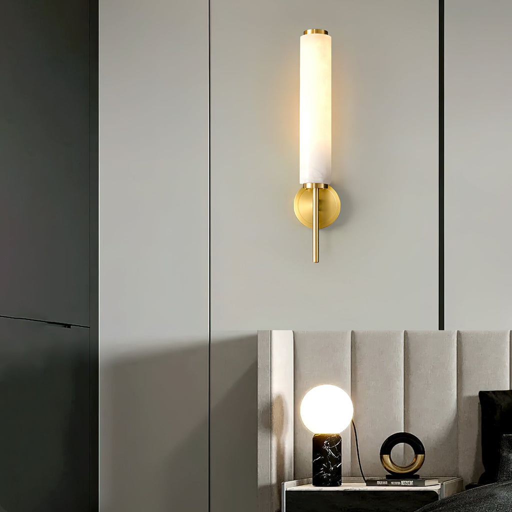 The Clérachic Olrinyra in brass lit on a panelled wall, above a bedside table set with a marble lamp.