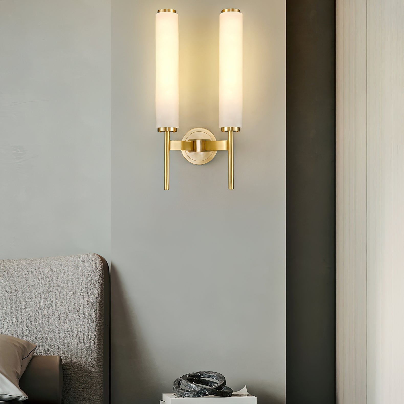 Clérachic Olrinyra twin in brass lit above an upholstered headboard, throwing a warm column up the wall.