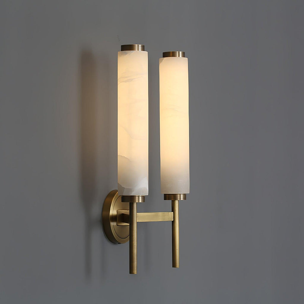 Clérachic Olrinyra twin in brass at three-quarter angle, both lit stone tubes casting soft shadow on grey.