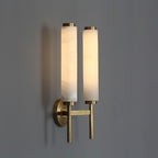 Clérachic Olrinyra twin in brass at three-quarter angle, both lit stone tubes casting soft shadow on grey.