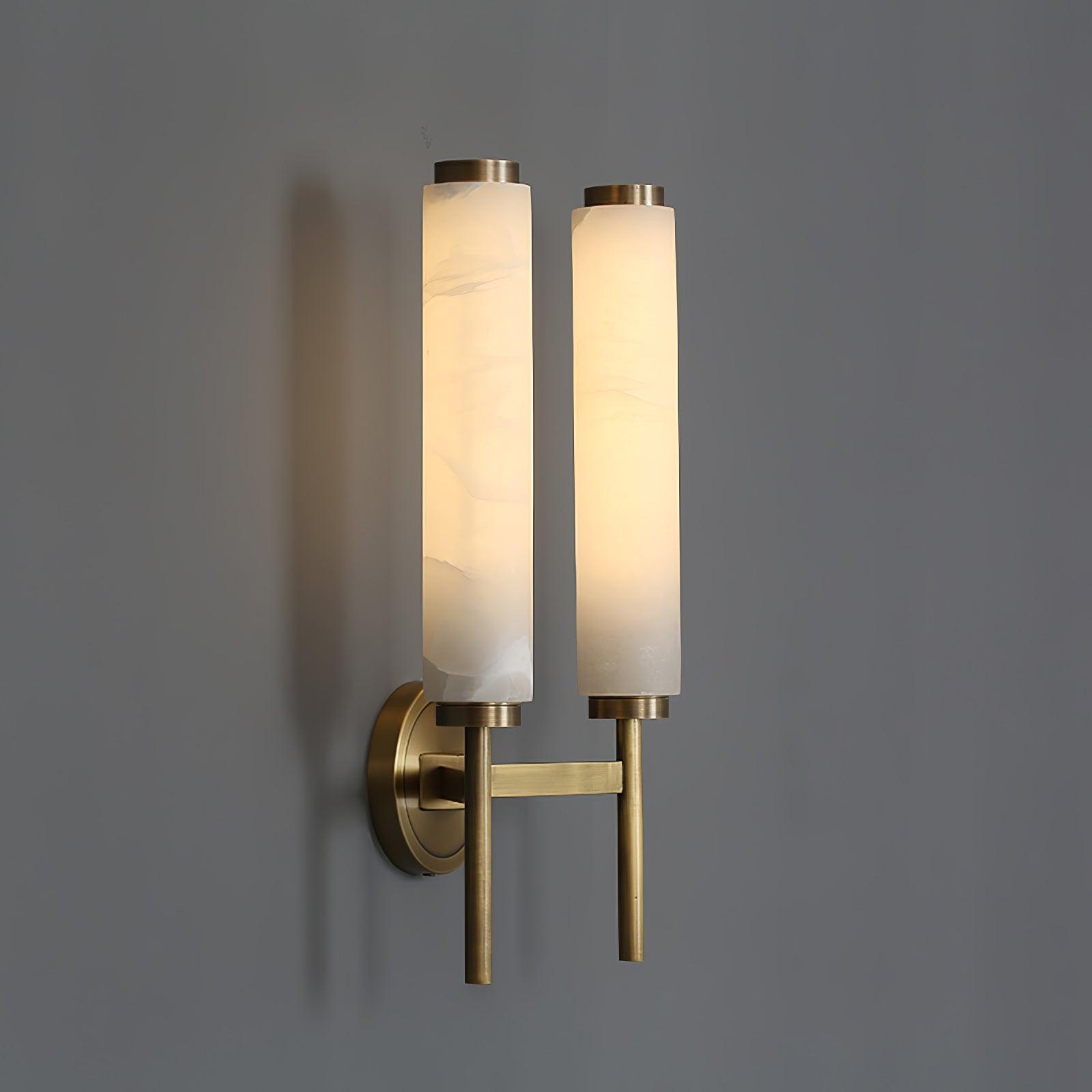 Clérachic Olrinyra twin in brass at three-quarter angle, both lit stone tubes casting soft shadow on grey.