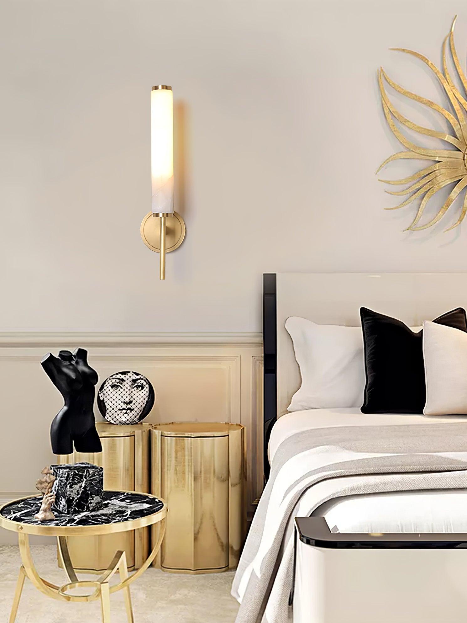 The Clérachic Olrinyra in brass lit in a bedroom, near a gilt sunburst piece above a marble side table.