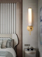 Clérachic Olrinyra in brass lit on a fluted wall panel beside an upholstered bed and round nightstand.