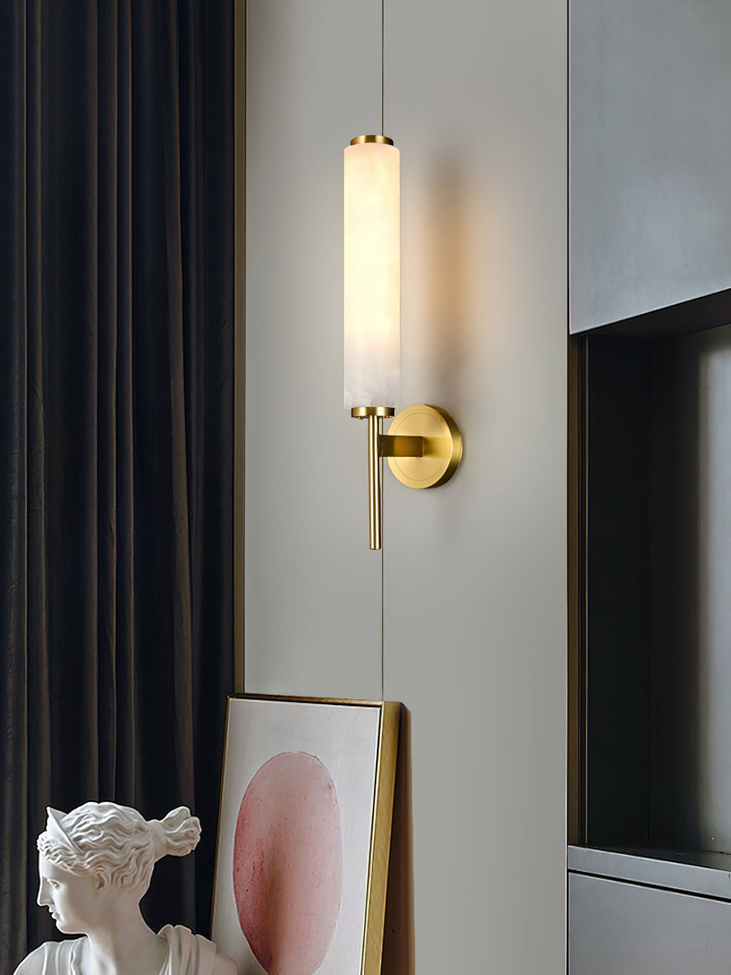 The Clérachic Olrinyra in brass lit beside a dark curtain, with a leaning framed print and plaster bust below.