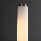 Clérachic alabaster cylinder lit against a charcoal wall, the stone's translucency and grain filling the frame.