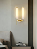 The Clérachic Olrinyra twin in brass lit above a bed, beside a side table stacked with books.