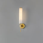 Clérachic Olrinyra in brass lit on a plain grey wall, the stone tube glowing evenly from base to tip.