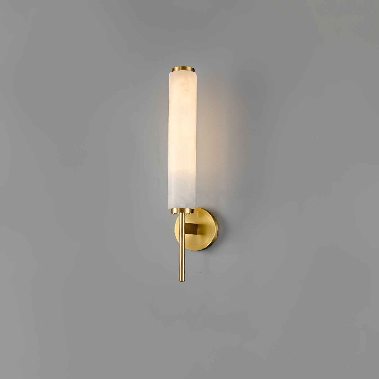 Clérachic Olrinyra in brass lit on a plain grey wall, the stone tube glowing evenly from base to tip.