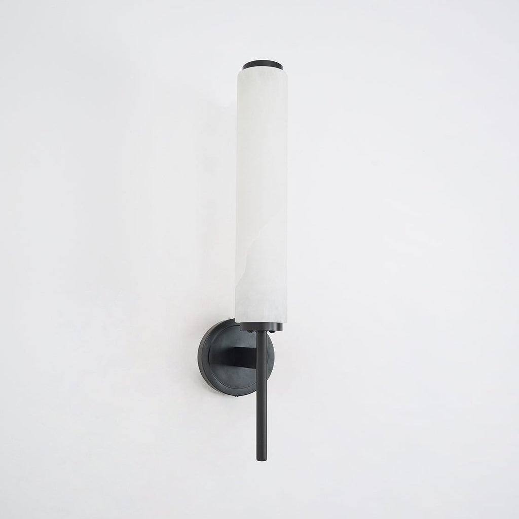 Clérachic Olrinyra in black unlit on a white wall, the alabaster tube cool and pale above the dark mount.